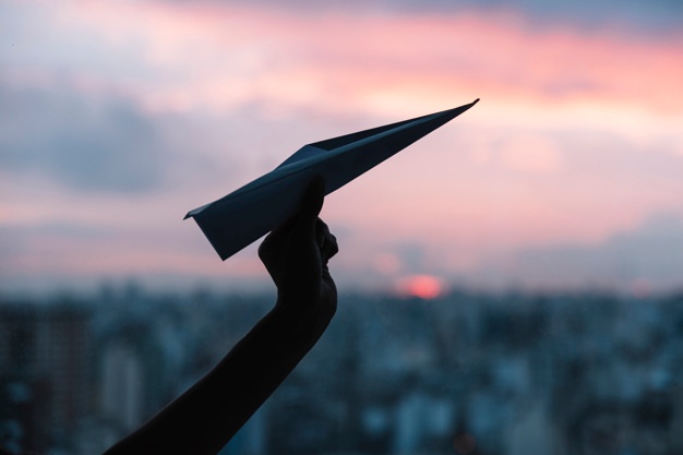silhouette-person-s-hand-holding-paper-airplane-against-dramatic-sky_23-2147958227